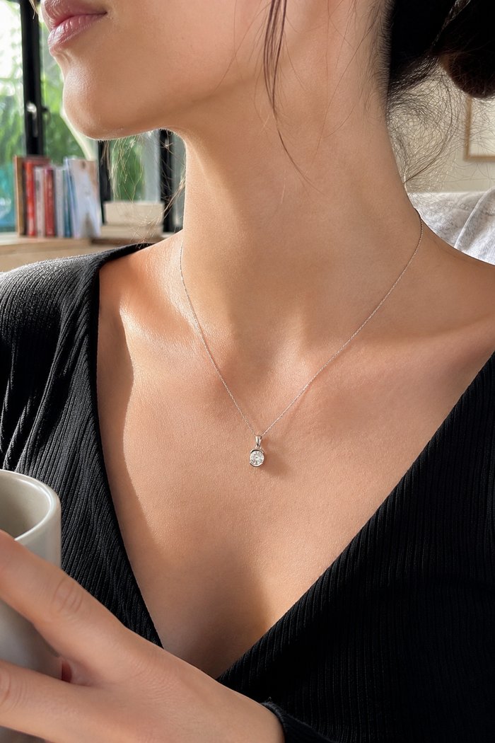A solitaire diamond pendant necklace styled into a café lifestyle scene